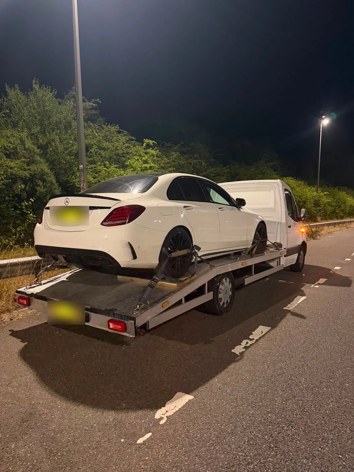 A white saloon strapped onto the bed of a recovery truck at night